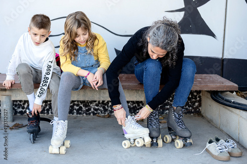 Adult woman helping children to wear roller skates photo