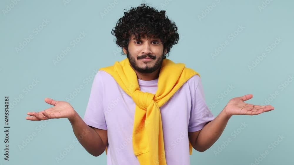 Fun confused shy shamed young bearded Indian man 20s wears violet t-shirt look camera spreading hands say oops ouch oh omg i am so sorry isolated on plain pastel light blue background studio portrait Fun confused shy shamed young bearded Indian man 20s wears violet t-shirt look camera spreading hands say oops ouch oh omg i am so sorry isolated on plain pastel light blue background studio portrait