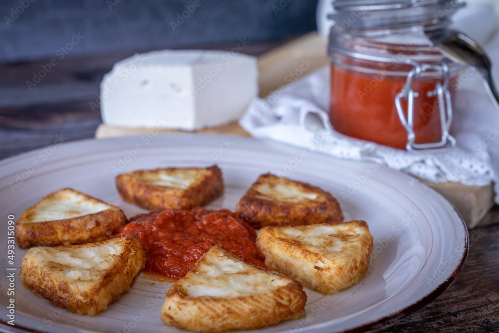 Fried goat cheese with tomato, a typical dish from the Region of Murcia, Spain, on a wooden background.