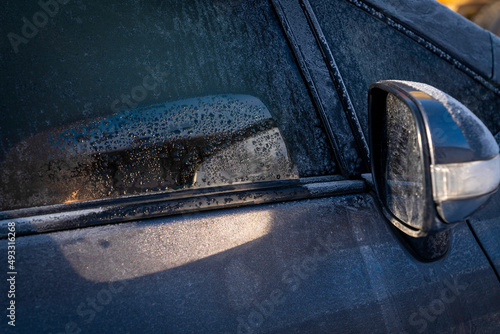 The sun hitting the mirror of the car on a winter day defrosts the hood of the car reflected by the mirror.