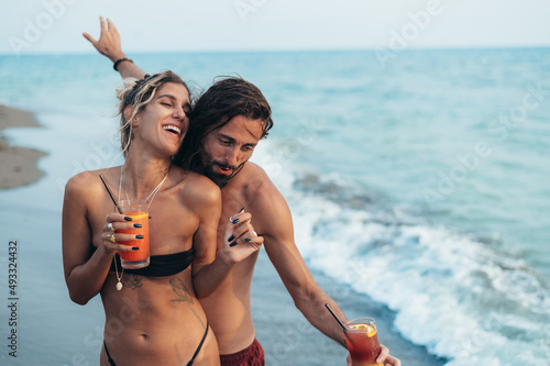 Attractive young couple with alcohol cocktails walking on the beach