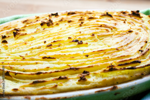 Delicious potato gratin with perfectly baked patterns on the surface, served in an oval ovenproof dish and placed on a bamboo kitchen board.
