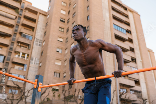 Determined shirtless African guy pulling up on bar photo