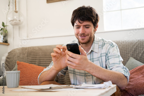 Portrait of man texting at home while doing paperwork photo