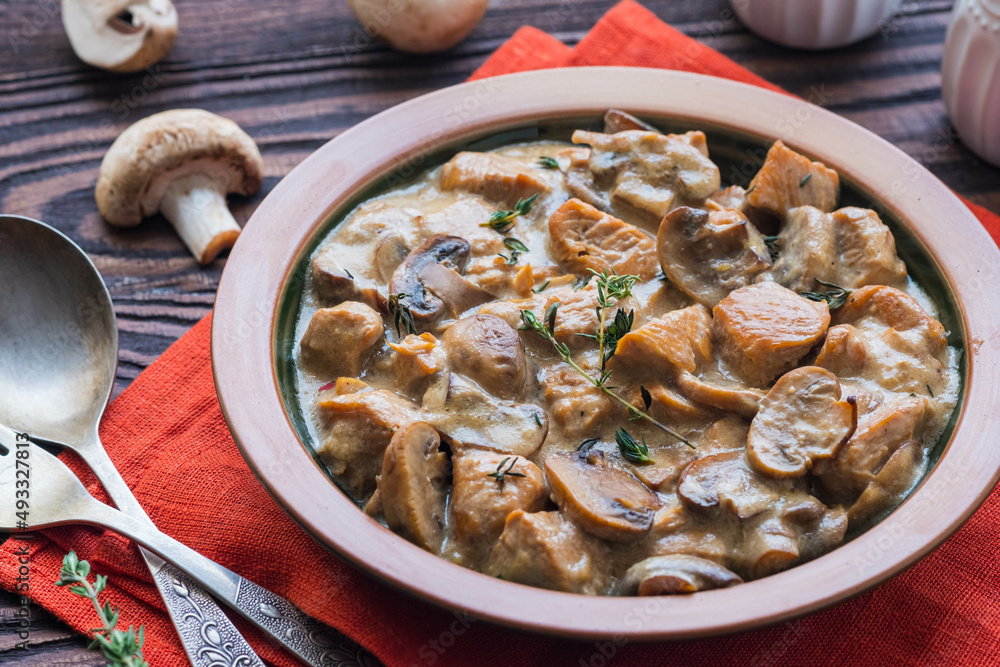 Stewed diced turkey with mushrooms in a creamy sauce in a clay plate on a brown wooden background. Turkey recipes.