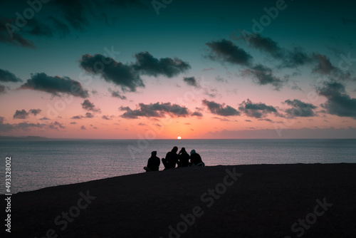 Sitting friends taking pictures at sunset photo