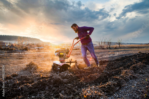 organic farming man cultivates the ground at sunset with a tiller  preparing the soil for sowing photo