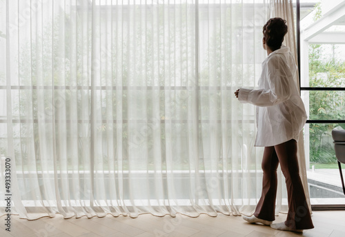 Woman opening sheer curtains in a large living room photo