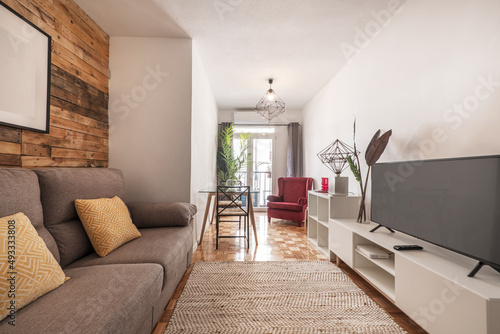 Salón decorado con paredes de madera sin barnizar en apartamento de alquiler a corto plazo con aparador blanco con tv y suelo de parquet de roble, alfombra de fibra y sillón rojo photo