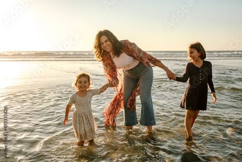 Mom and girls wading in ocean at sunset photo