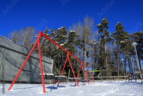 Red swing set during the winter. Plenty of snow on the ground. Sunny day with a blue sky. Stockholm, Sweden, Scandinavia, Europe.