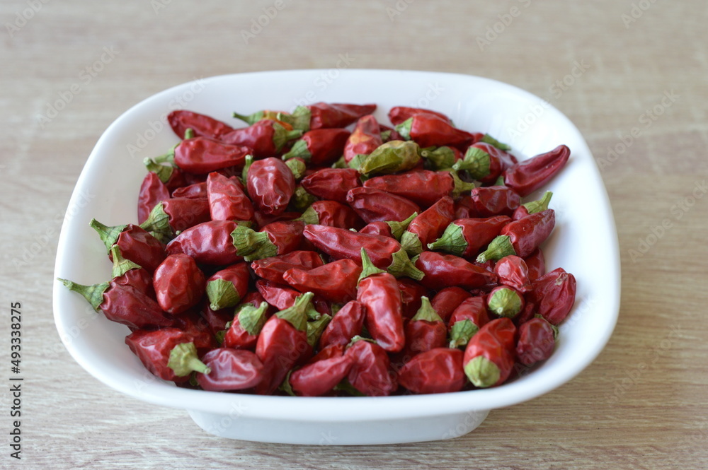 small extremely hot red peppers in a white bowl on a wooden table small extremely hot red peppers in a white bowl on a wooden table