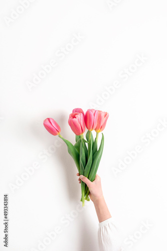 Girl's hand holding bouquet of beautiful pink tulip flowers on white background
