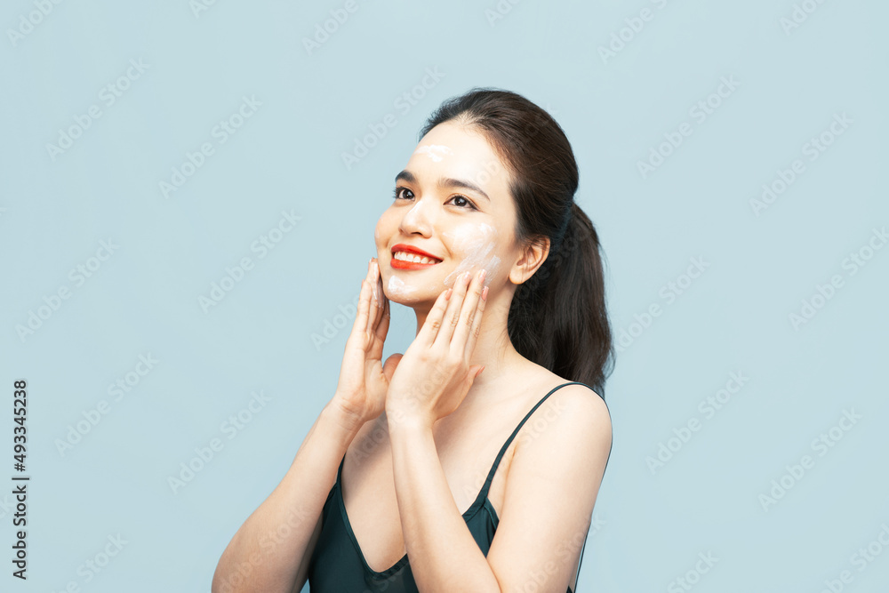 woman applying face cream and looking away isolated over light blue background woman applying face cream and looking away isolated over light blue background