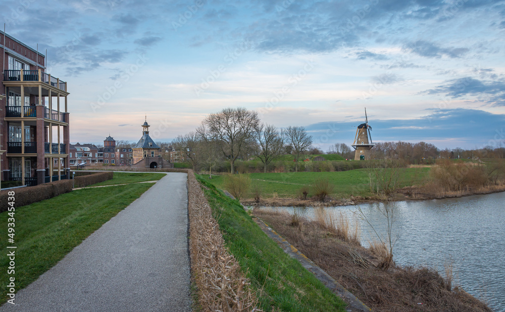 Pedestrian path along the historical fortifications in dutch city of Gorinchem with a view on windmill and an old city gate