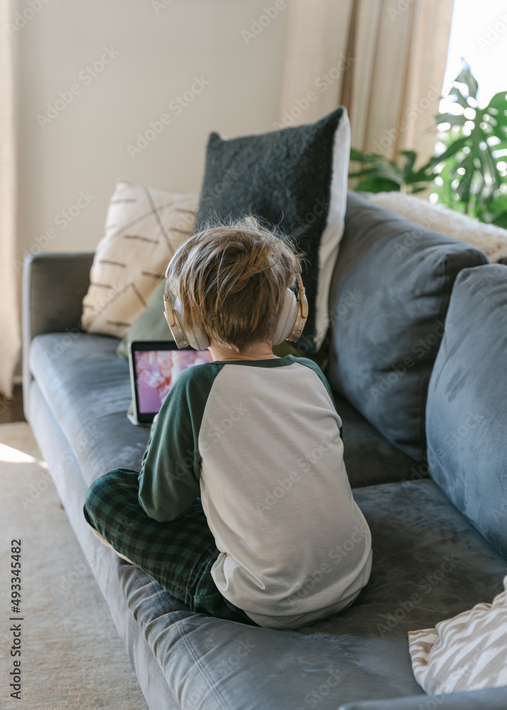 Boy in pjs with headphones on watching ipad Boy in pjs with headphones on watching ipad