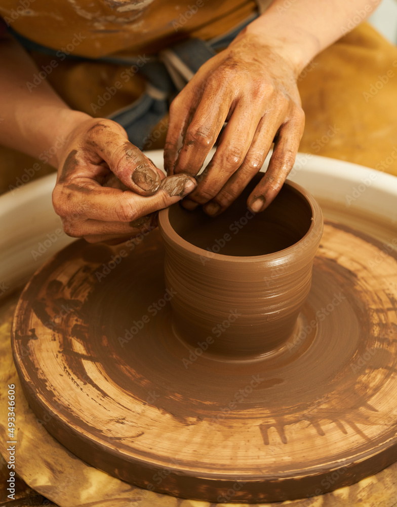 A Potter works with red clay on a Potter's wheel in the workshop..Women's hands create a pot. Girl sculpts in clay pot closeup. Modeling clay close-up. Warm photo atmosphere. 