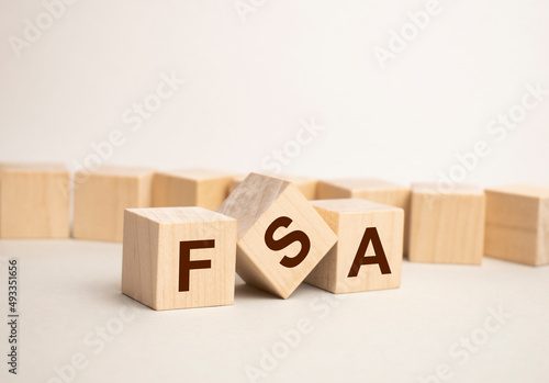 letters of the alphabet of FSA on wooden cubes, green plant on a white background. FSA - short for Flexible Spending Account