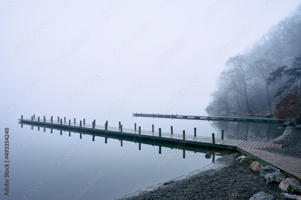 Jetty and trees on Lake Windermere in fog at dawn Jetty and trees on Lake Windermere in fog at dawn