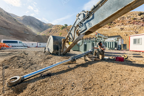 Repairman is repairing to hydraulic piston of the excavator with covered elektrode in the construction site. Excavators are heavy construction equipment consisting of a boom, dipper (or stick). photo