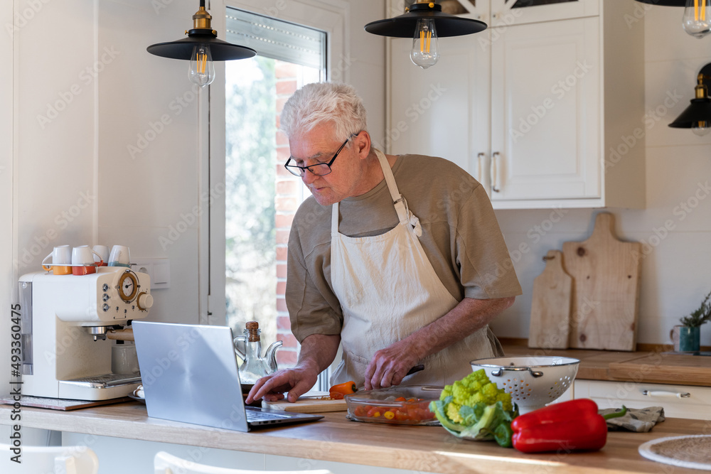 Senior man cooking with online tutorial on laptop Senior man cooking with online tutorial on laptop