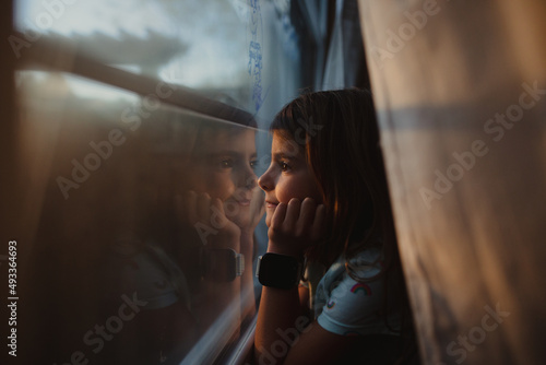 Young girls looks out window with sun setting outside  photo