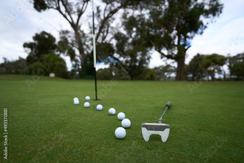 A golf putter and line of balls on a golf course green photo
