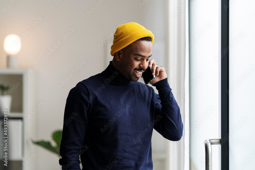Modern man in bright hat talking on smartphone at home Modern man in bright hat talking on smartphone at home