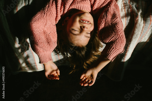 girl smiles at camera while hanging head off edge of bed in sunshine photo