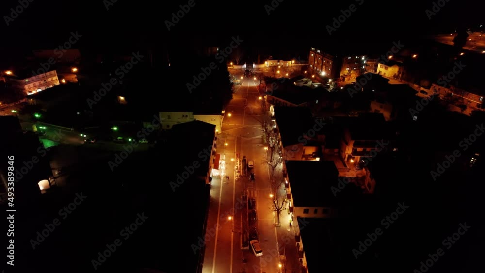 Forward aerial view of a street and a square lit yellow in the night. Forward aerial view of a street and a square lit yellow in the night.