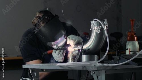 A fabricator TIG welding stainless steel exhaust pipe with pie cuts. 
Static shot from far away. photo