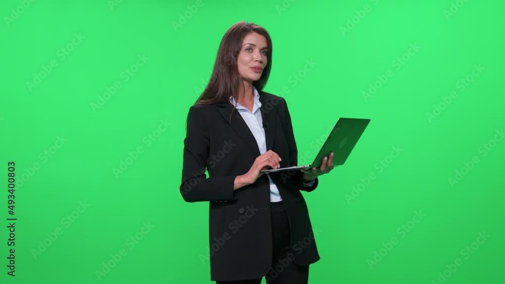Woman lecturer in suit speaks to the audience and give a lecture using a laptop, green background. Woman lecturer in suit speaks to the audience and give a lecture using a laptop, green background.