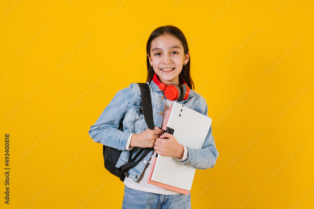 portrait of young hispanic child teen girl student with headphones listening music on a yellow background in Mexico Latin America portrait of young hispanic child teen girl student with headphones listening music on a yellow background in Mexico Latin America