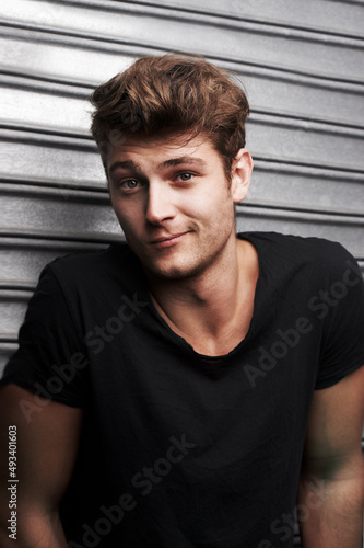 Hes hasnt a care. Portrait of a handsome young man standing in front of some metal shutters.
