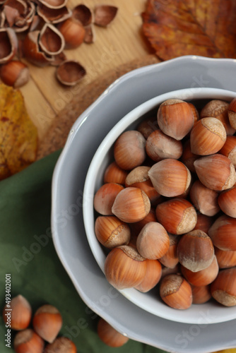 Whole hazenuts in a bowl with cracked hazenuts and autumnal leaves on wooden background