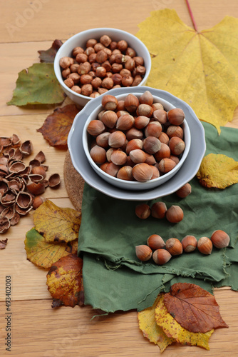 Whole hazenuts in a bowl with cracked hazenuts and autumnal leaves on wooden background photo