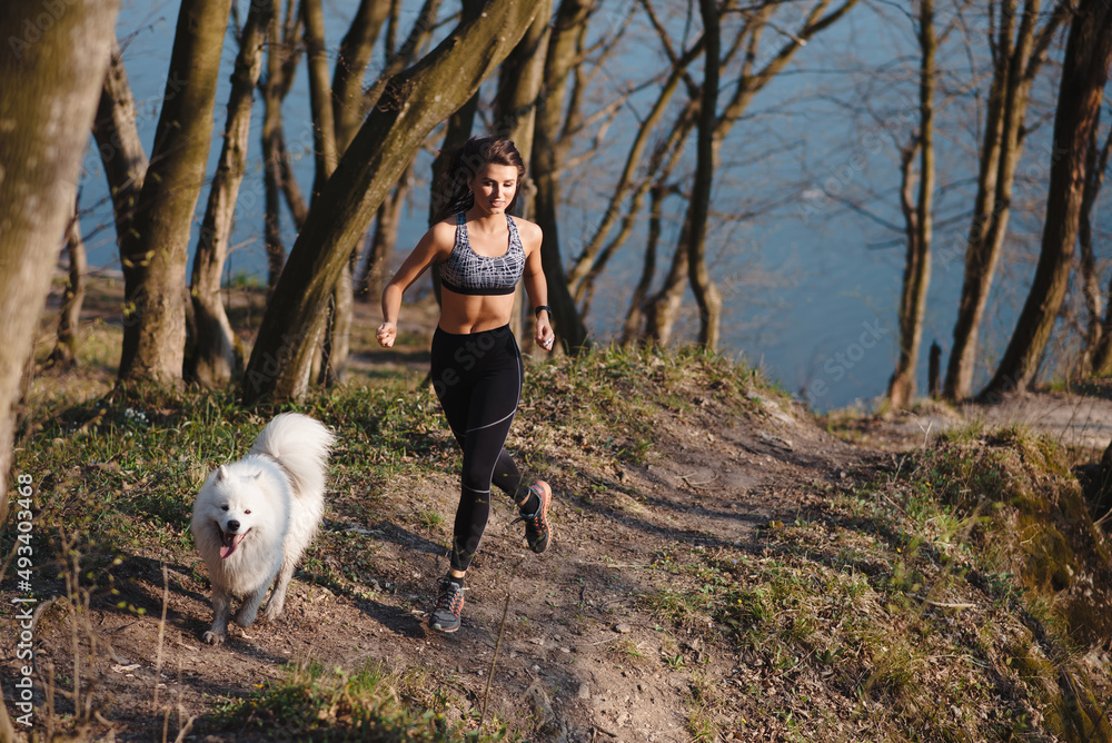 Athletic woman running with white fluffy dog outdoors