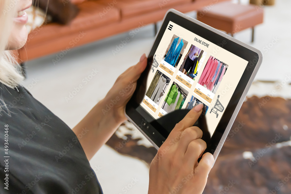 Technologies make business easier. Beautiful young woman using her digital tablet with smile while standing at the clothing store.