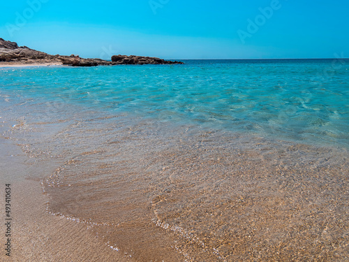 smooth waves of a turquoise sea gently touch the sandy beach under the crystal clear blue sky.