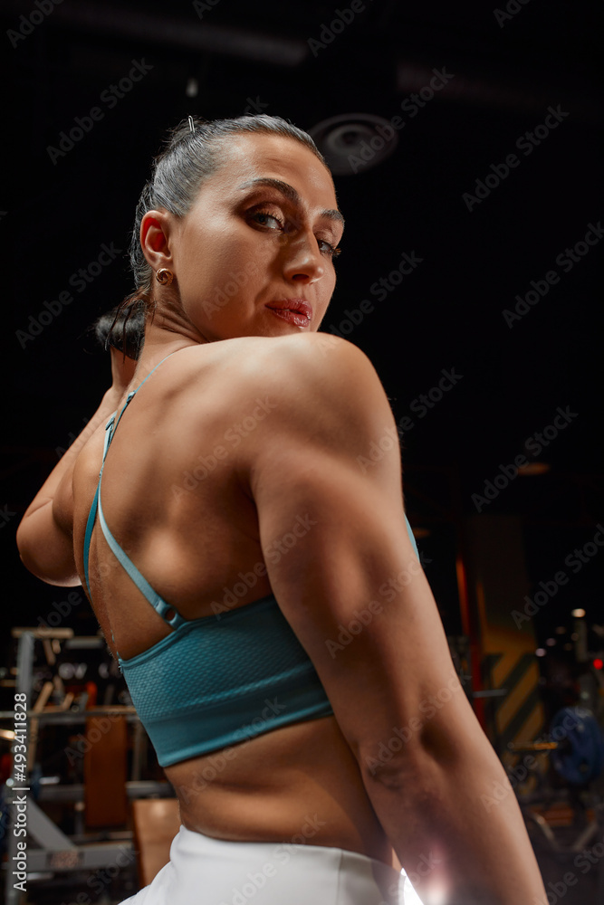 Muscular woman in gym showing back muscles. - Stock Photo