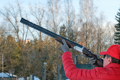 athlete in a red baseball cap and jacket shoots a double-barreled shotgun