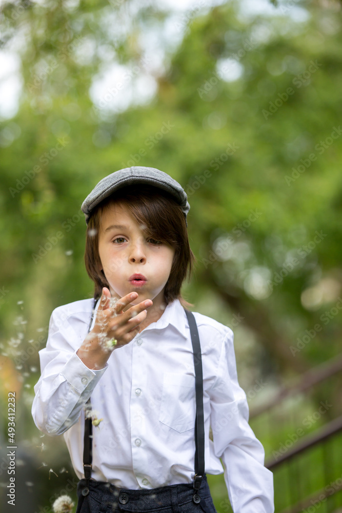 Child in retro clothing, wearing hats, suspenders and white shirt, blowing dandelions Child in retro clothing, wearing hats, suspenders and white shirt, blowing dandelions