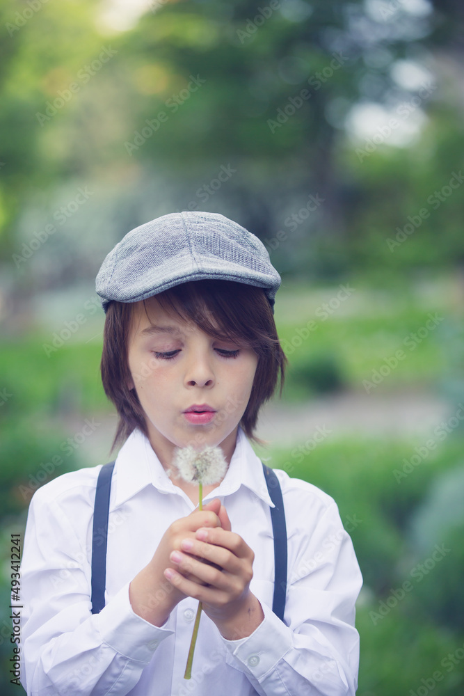 Child in retro clothing, wearing hats, suspenders and white shirt, blowing dandelions Child in retro clothing, wearing hats, suspenders and white shirt, blowing dandelions
