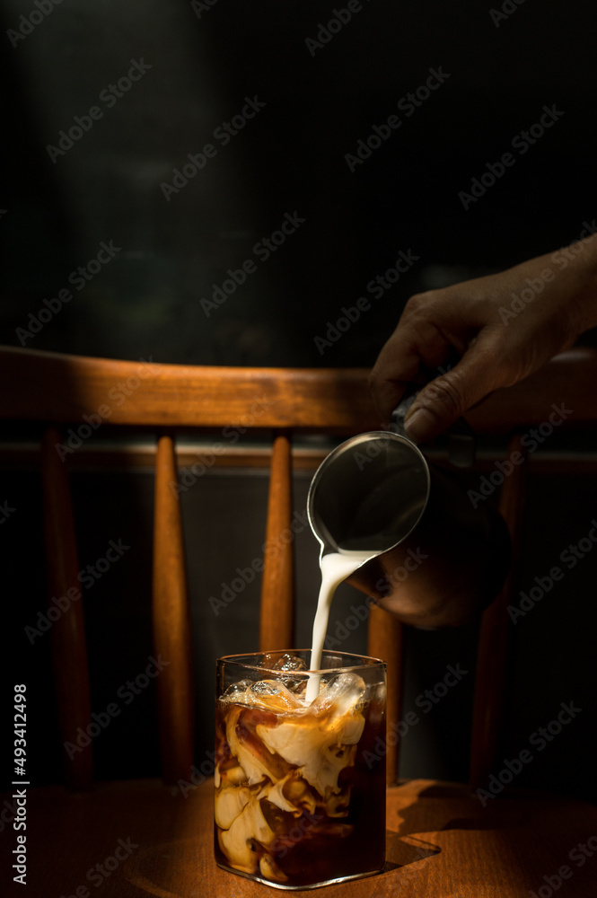 Ice coffee on a wooden table with cream being poured into it showing the texture and refreshing look of the drink