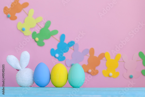 White bunny toy with colorful eggs and decoration on pink Easter background.