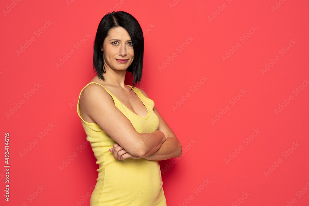 Portrait of positive beautiful middle aged woman with black hair in yellow dress . indoor studio shot isolated on red. Portrait of positive beautiful middle aged woman with black hair in yellow dress . indoor studio shot isolated on red.