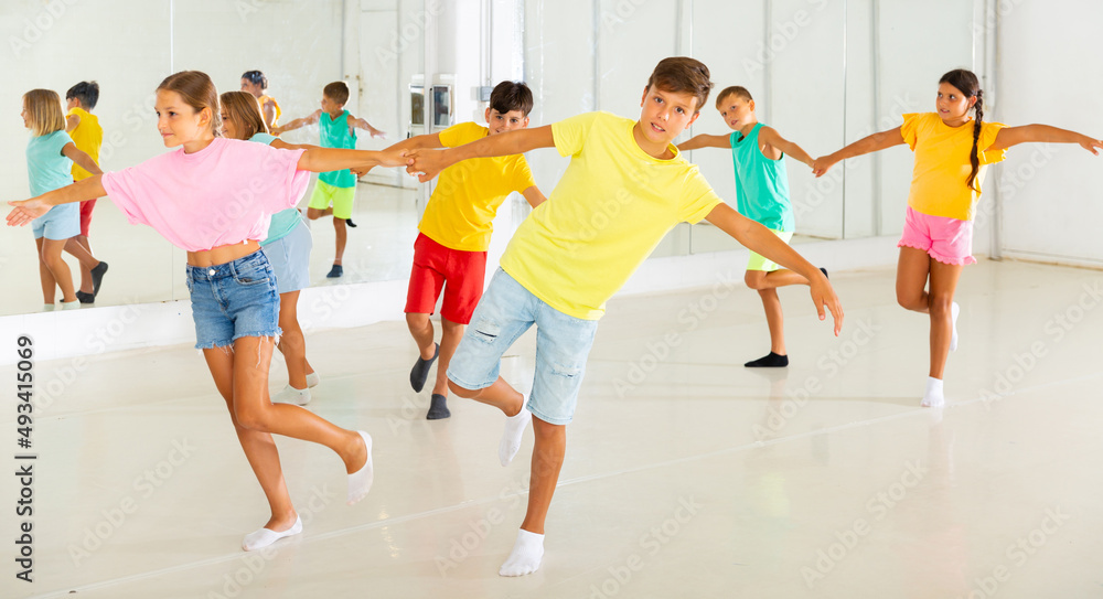 Young boys and girls holding each other hands while dancing in pairs in studio.