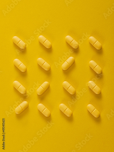 Pills in a row on yellow background. Vertical composition..