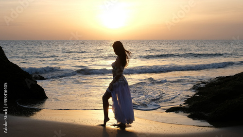 Woman looking at the sun at sunset on the beach stylized in belly dancer clothes. Woman dances to the sun wearing arabic dance costume. Fertility concept. Exotic beauty.