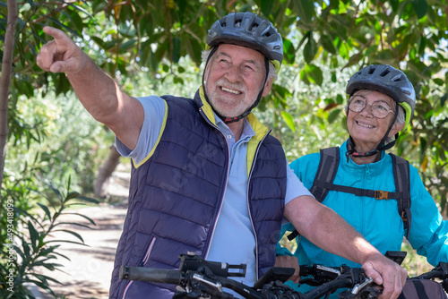 Active senior couple with electrobikes standing outdoors in the park. Two happy elderly people running in nature with their bicycles enjoying healthy lifestyle #493418093